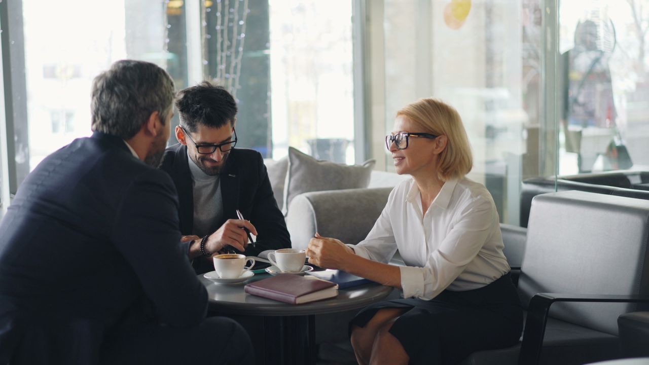 Mastering the First Impression: Your intriguing post title goes here Three professionals engaged in a business meeting at a cafe.